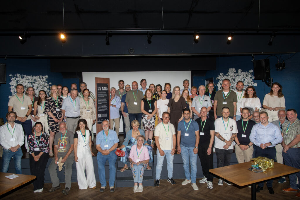 Large group of people with lanyards posing on a stage indoors for a group photo.