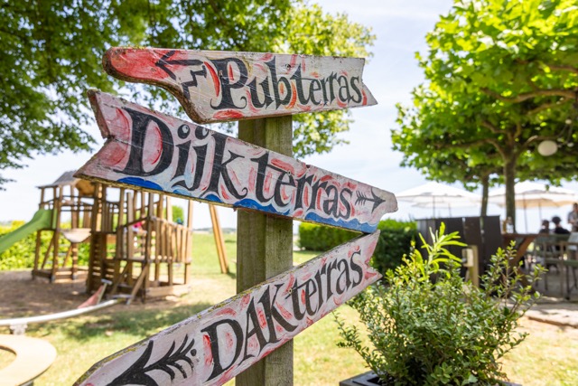 Wooden signpost with three colorful arrow signs in a sunny outdoor park area with a playground nearby.