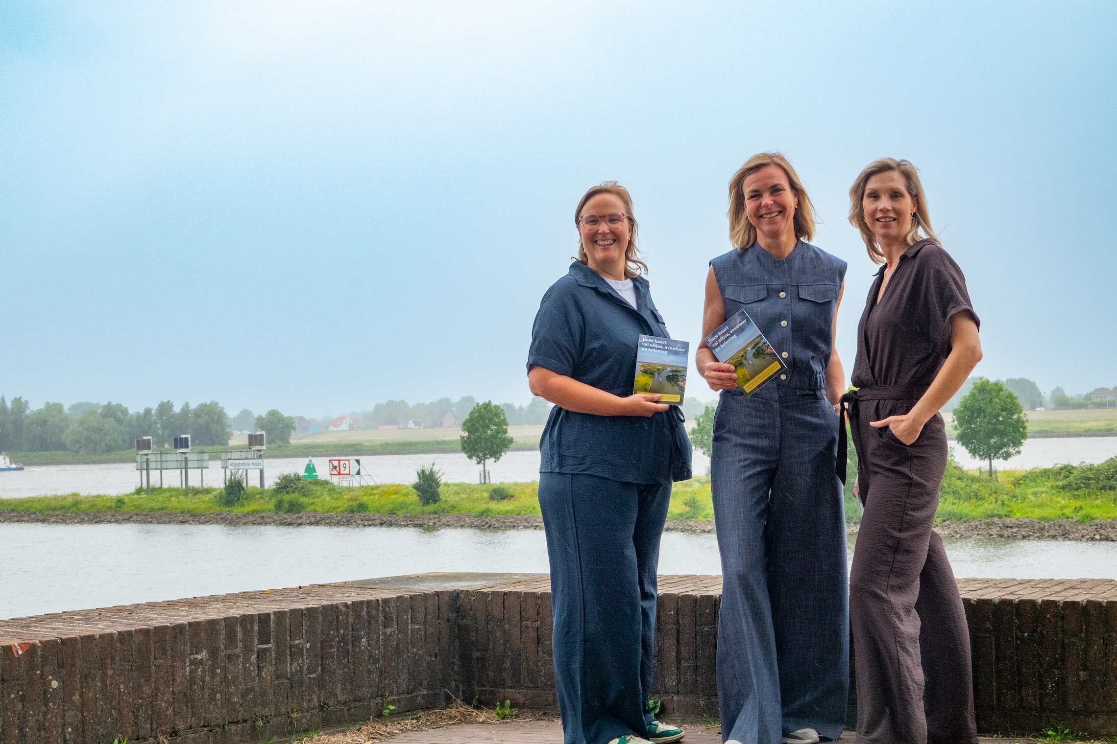 LR--09323 - Stichting Bureau Toerisme - Stichting Bureau Toerisme Three women stand by a lake, smiling at the camera and holding brochures.