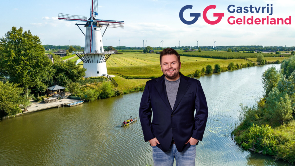 Smiling man in a navy blazer stands by a river with a windmill and fields behind him; Gasvrij Gelderland logo.